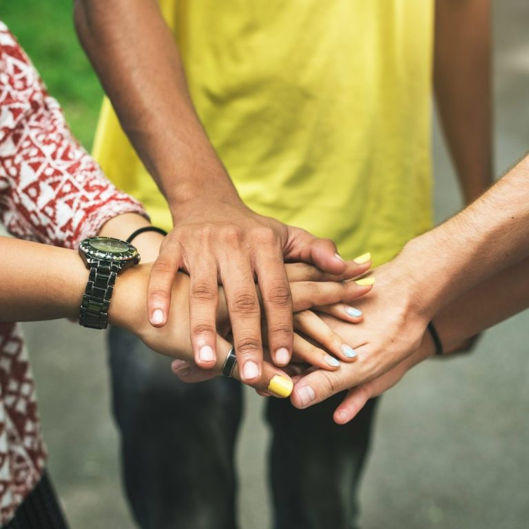 Several hands of different individuals stacked together in a show of unity.